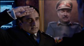 Colonel Ahmed salutes the Doctor in front of a portrait of the late Brigadier Lethbridge-Stewart
